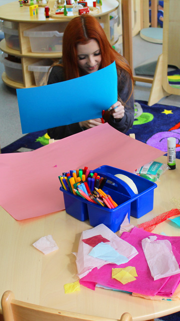 Education and early years student cuts paper shapes in simulated nursery