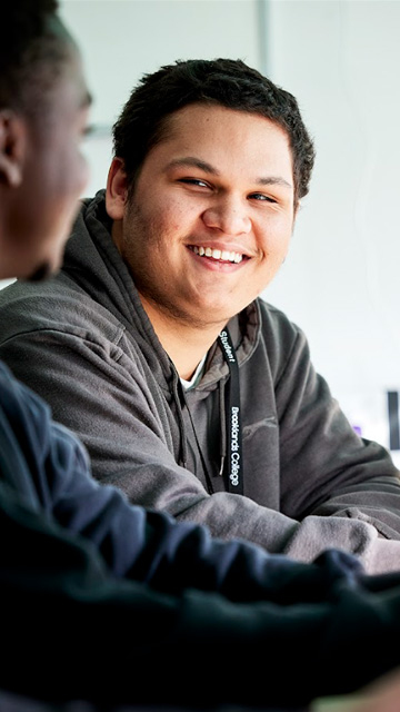 Smiling student wearing a Brooklands College hoodie, talking with another student