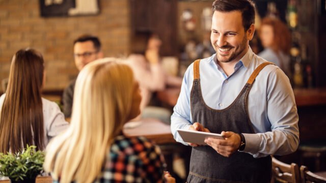 Happy waiter serves customer with tablet in hand