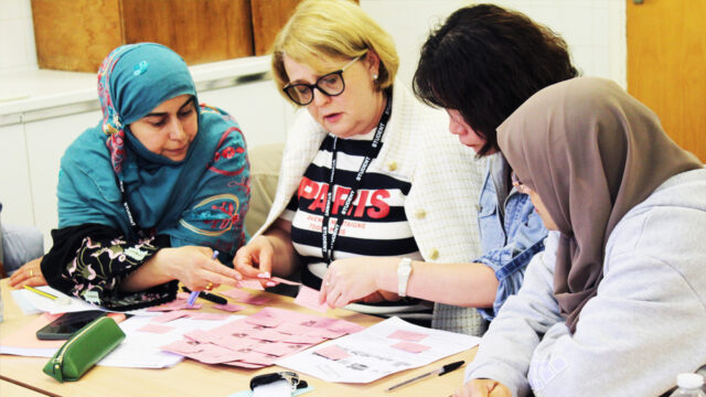 Four students collaborating around a table covered with pink cards and worksheets in a classroom setting