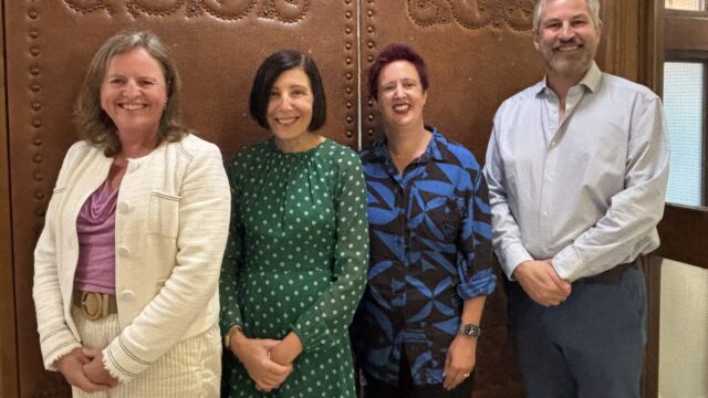 Four people smiling and posing together in front of an ornate embossed leather wall panel