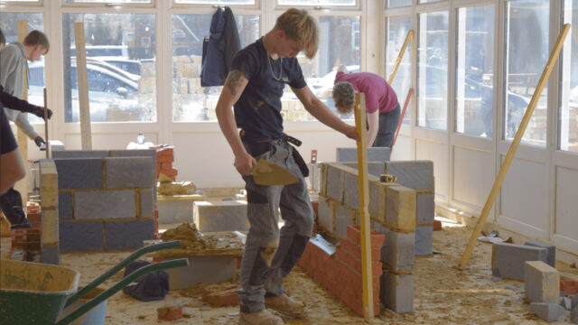 Bricklaying students build walls in construction workshop