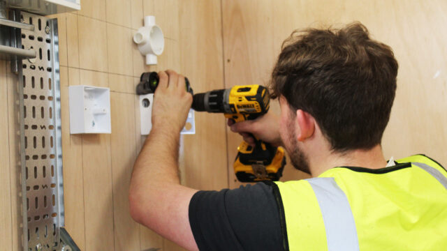 Electrical student drills into wall in workshop