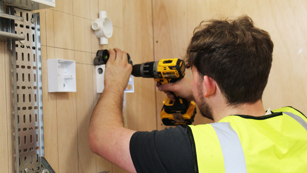 Electrical student drills into wall in workshop