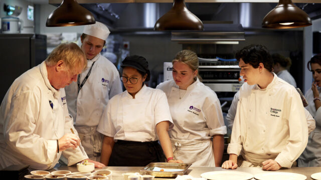 A chef instructor demonstrates plating techniques to Brooklands College catering students in a professional kitchen
