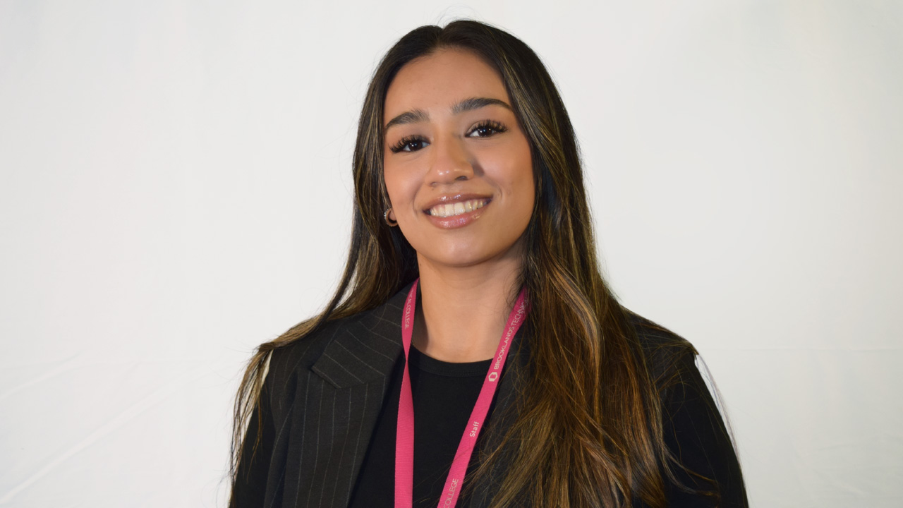 A smiling female staff member wearing a black blazer and a pink Brooklands College staff lanyard