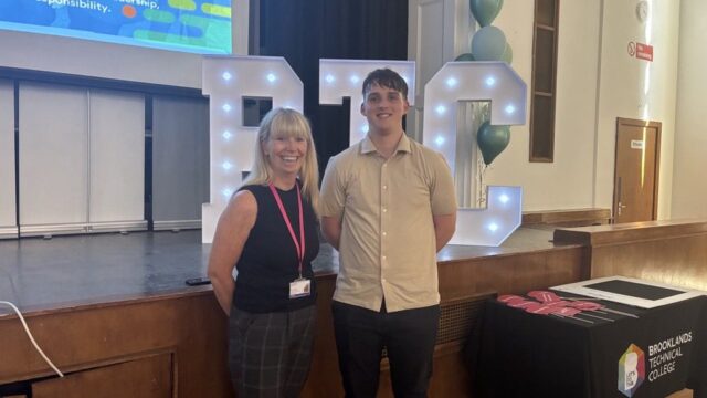 Two people posing together at a Brooklands Technical College event, standing in front of illuminated BTC letter decorations and green balloons