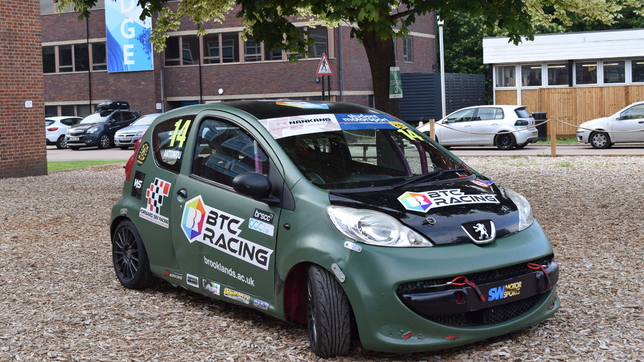 BTC Racing-liveried Peugeot 107 race car number 14, sponsored by Brooklands College, displayed on a campus grounds