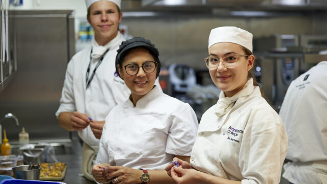 Three catering students smiling while preparing food to be served at Brooks Restaurant