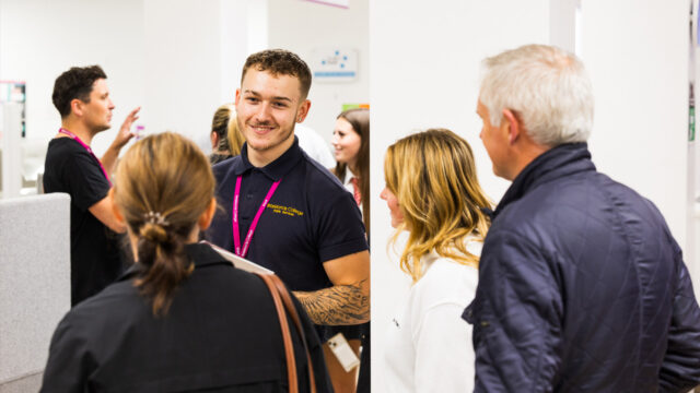 A Brocklands College Public Services student in a branded polo shirt and lanyard speaking with visitors at an open day event